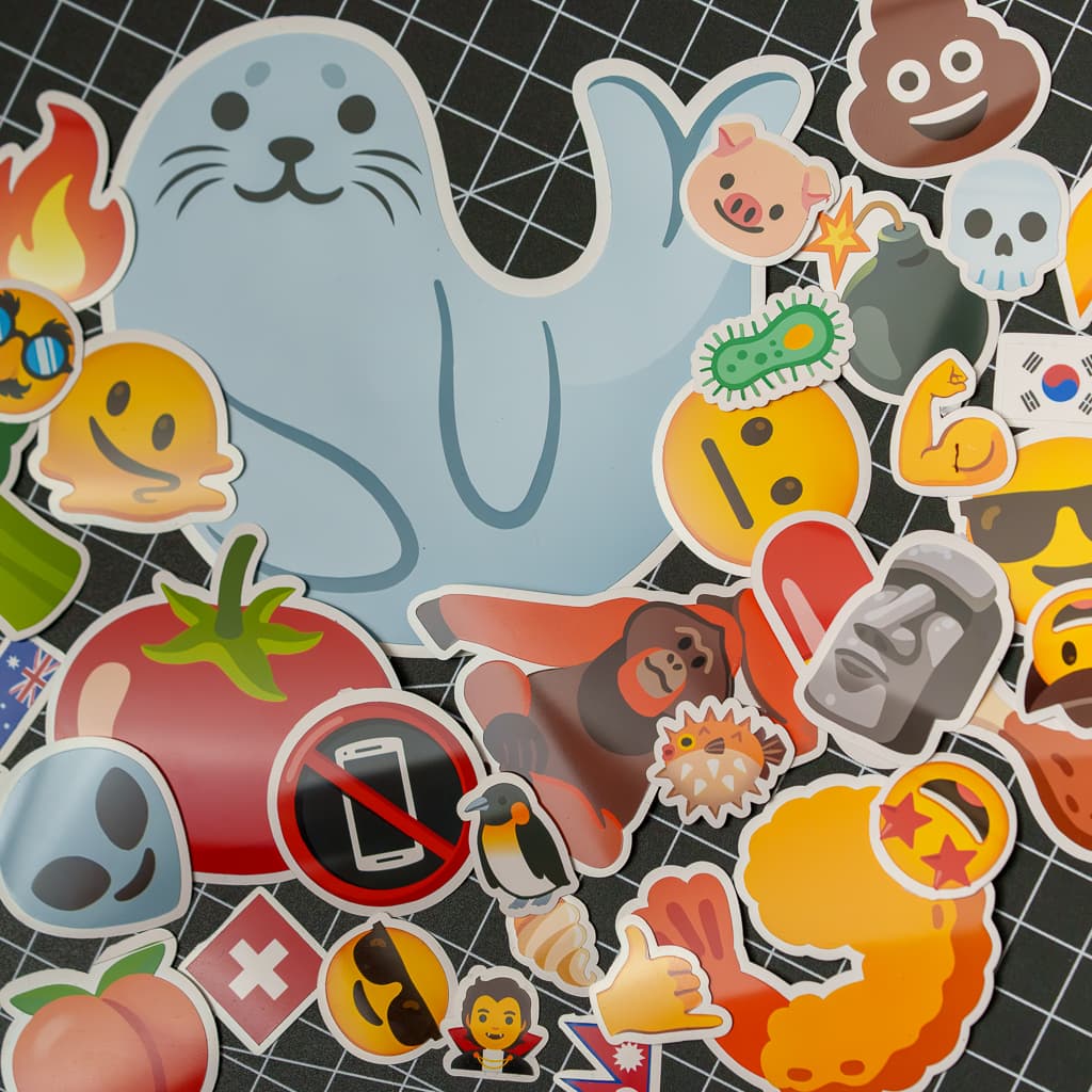 A collage of die-cut stickers, including a seal, a tomato, and a skull, laid out on a cutting mat