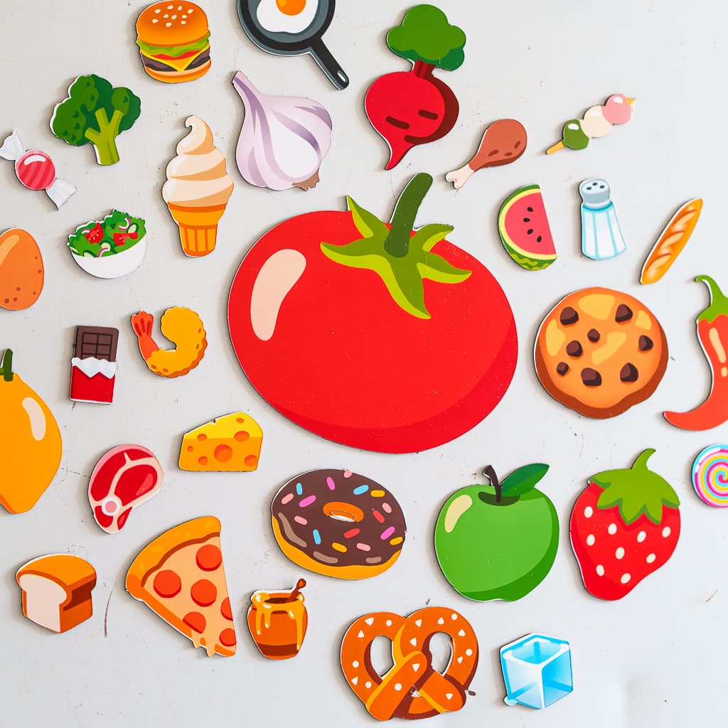 A collage of die-cut food magnets, including a tomato, a burger, and a strawberry, on a white fridge surface