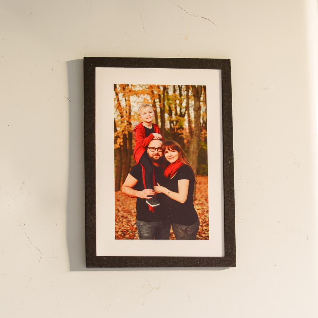 A framed magnet with a family portrait photo in a black cardstock frame, hung on a wall